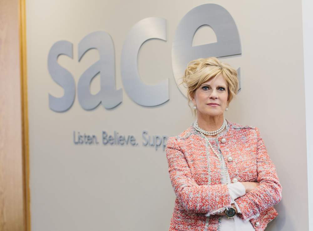 Mary Jane James stands in front of a sign that says "SACE. Listen. Believe. Support."