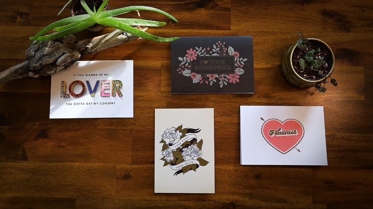 Four SACE consent-themed greeting cards displayed on a dark brown wood table with plants.