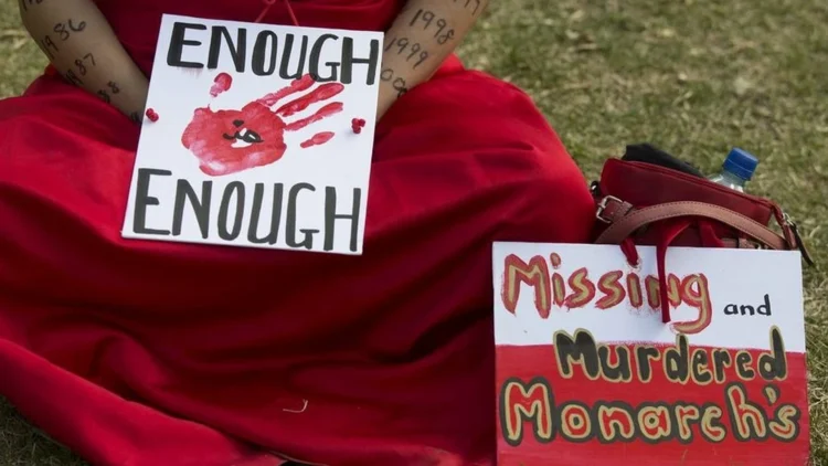 Picture of an indigenous person in a red dress, holding a sign that says "Enough is enough"