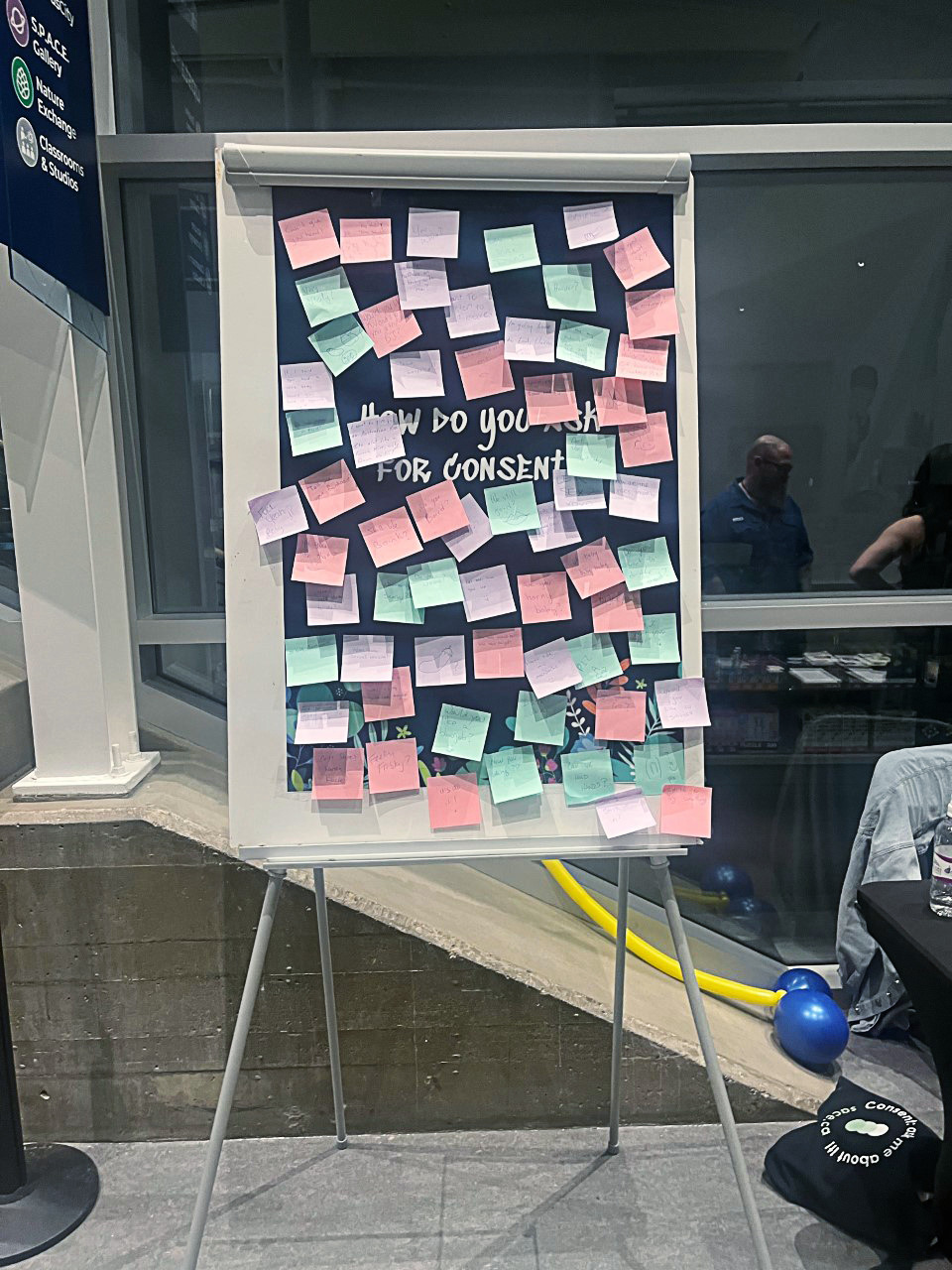 A giant board that invites the public to write down the ways they communicate consent, covered in sticky notes.