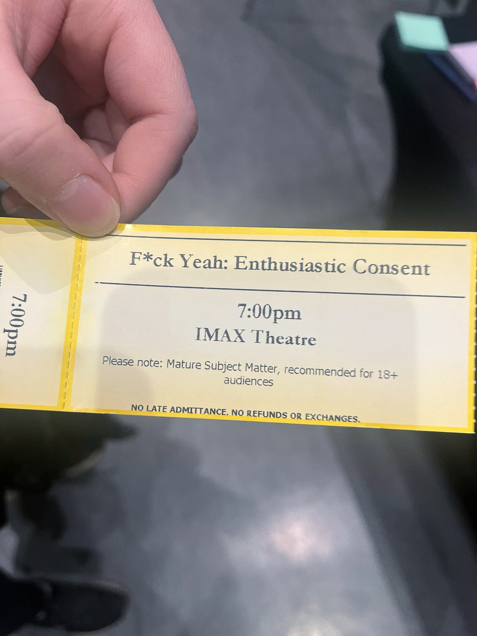 A person holding up an admission ticket to the event that reads "F*ck Yeah Enthusiastic Consent" 7:00pm IMAX Theatre