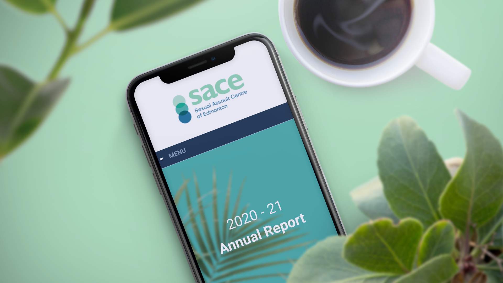 A cell phone displaying the 2020-2021 Annual Report from the SACE website on a mint green background, plants and a cup of coffee.