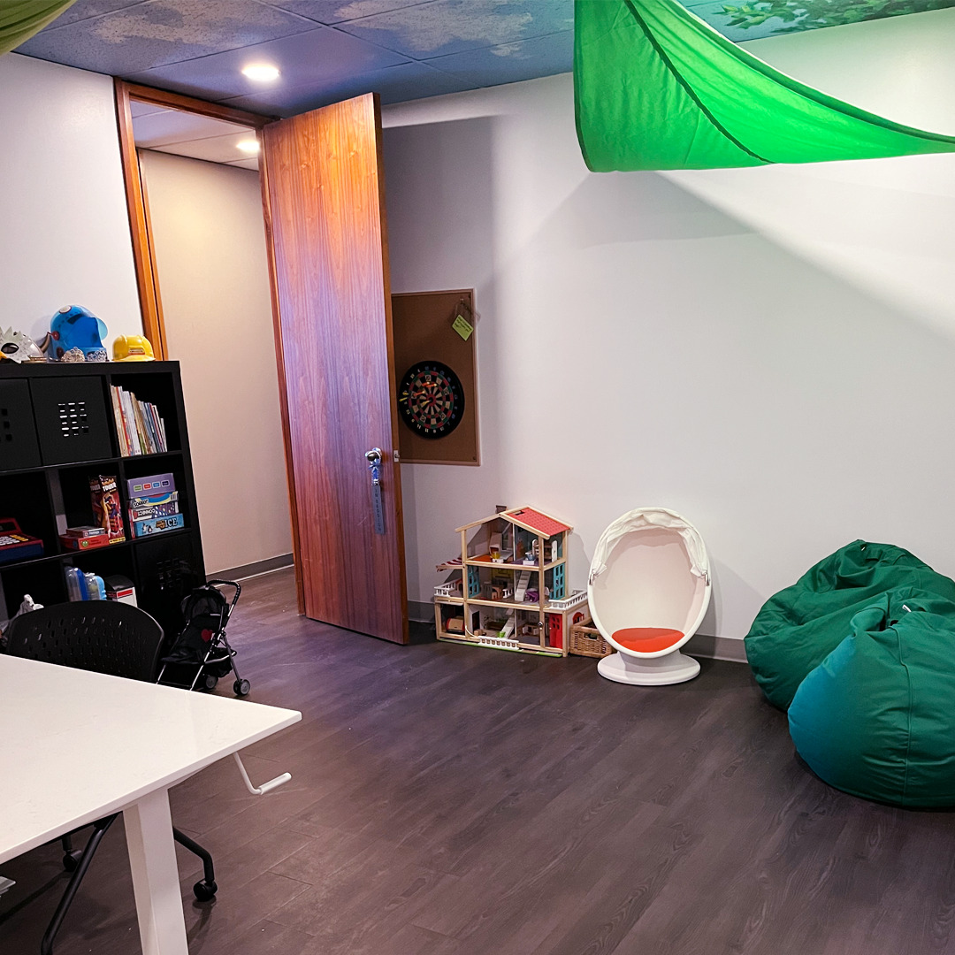 SACE playroom entrance with bean bags, shelf of play therapy toys and a playhouse for dolls.