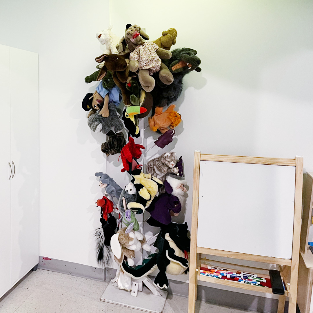 A photo of the child and youth counselling playroom shows an easel and rack full of puppets used for therapeutic play
