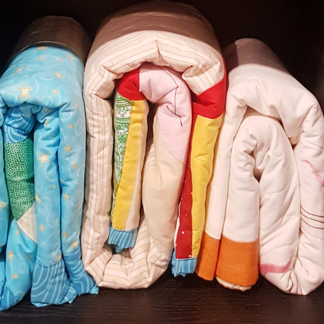 Folded quilts stored in a SACE cubby ready for the child counselling program. Sewing quilts is one of the unique ways to give to SACE.